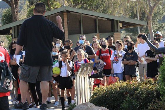 Coach with a soccer ball addressing a large crowd of masked young players