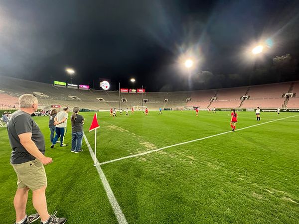 Field-level view of the lit Rose Bowl at night with a corner flag in the foreground and play in progress