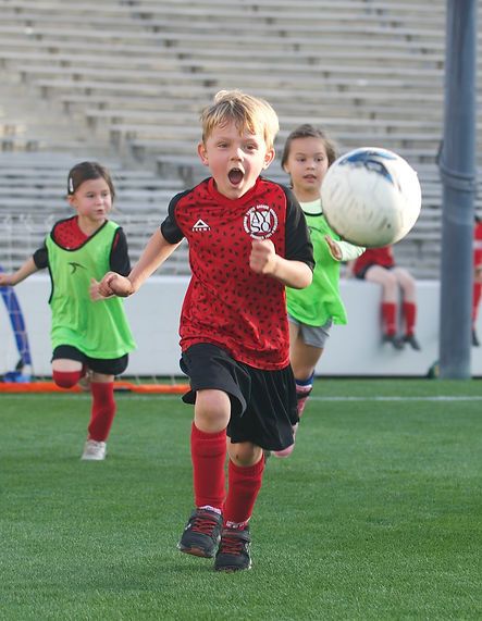 Boy in a red AYSO jersey sprinting after the ball with mouth open in excitement