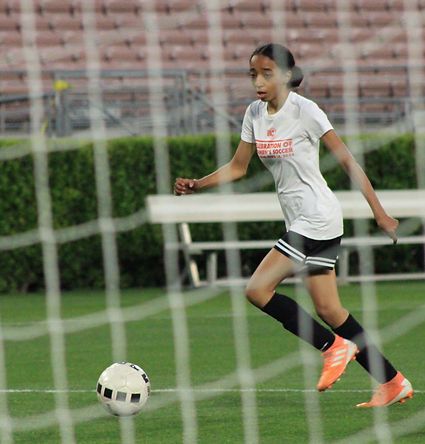 Teen player in a white Celebration shirt dribbling along the goal line