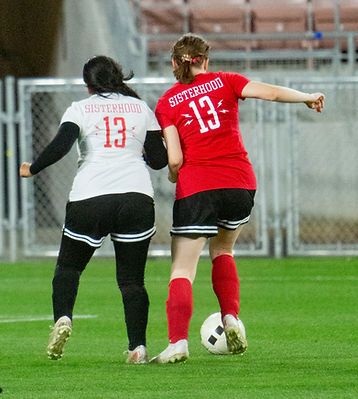 Two players in red and white Sisterhood number 13 jerseys battling for the ball, viewed from behind