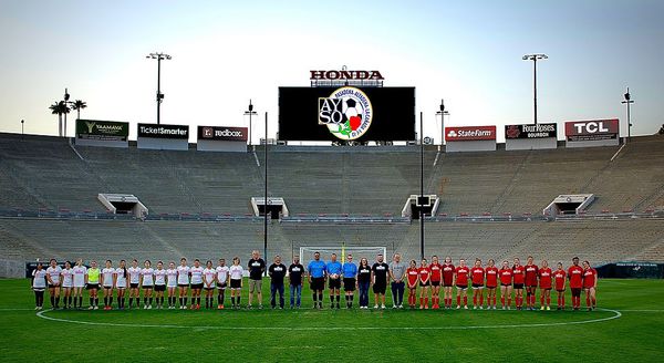 Wide-angle view of both exhibition teams and officials at midfield with the AYSO Region 13 logo on the Rose Bowl jumbotron