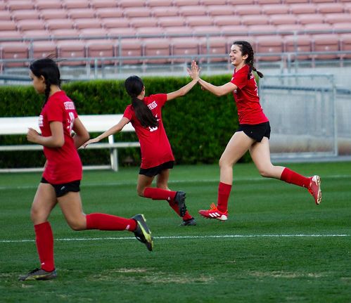 Three players in red Region 13 shirts celebrating; one leaping for a high-five