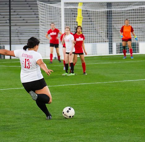 Player in a white Sisterhood 13 jersey shooting at goal as defenders converge