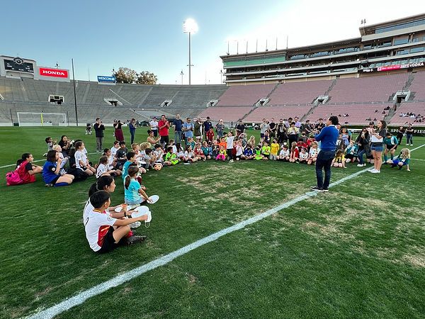Cobi Jones speaking to kids seated in a circle on the Rose Bowl pitch