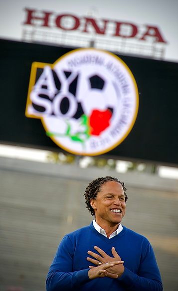 Cobi Jones smiling with the AYSO Region 13 logo on the Rose Bowl jumbotron behind him