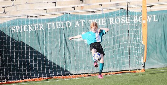 Girl kicking a soccer ball in front of the Spieker Field at the Rose Bowl banner