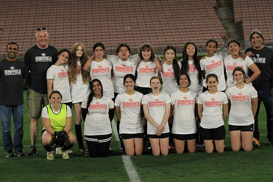 Team photo of older girls and coaches in white Celebration of Women's Soccer t-shirts