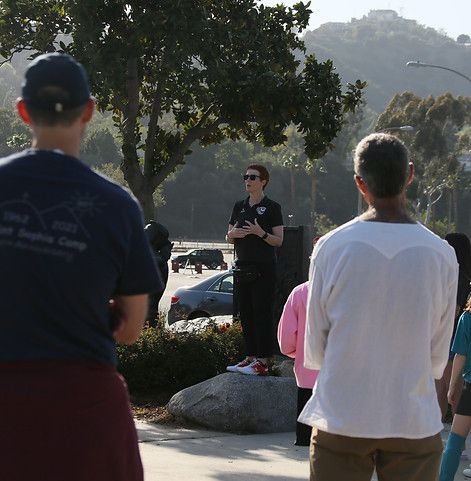 Woman speaking to a crowd of kids and parents on a sunlit walkway