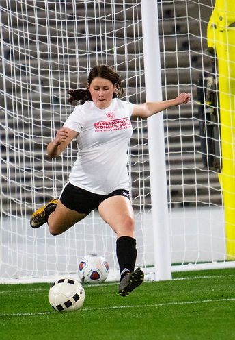 Teen player in a white Celebration t-shirt striking the ball at the goal mouth