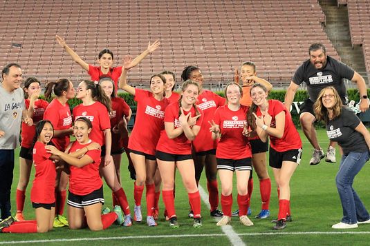 Group of teen girls in red Region 13 shirts cheering and posing on the Rose Bowl pitch