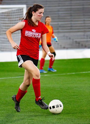 Teen player in a red Celebration of Women's Soccer t-shirt dribbling on the field