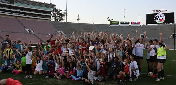 Large group of kids on the Rose Bowl pitch with arms raised, cheering